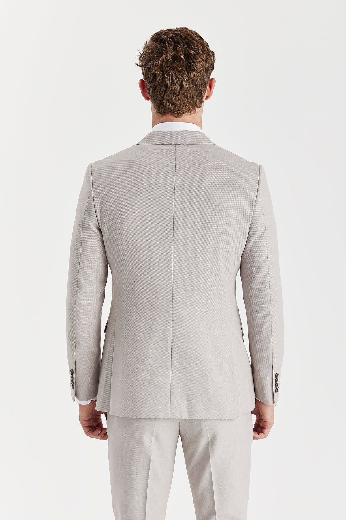 Rear view of the stone jacket showing its centre seam, shaped waist, twin back vents and brown cuff buttons.