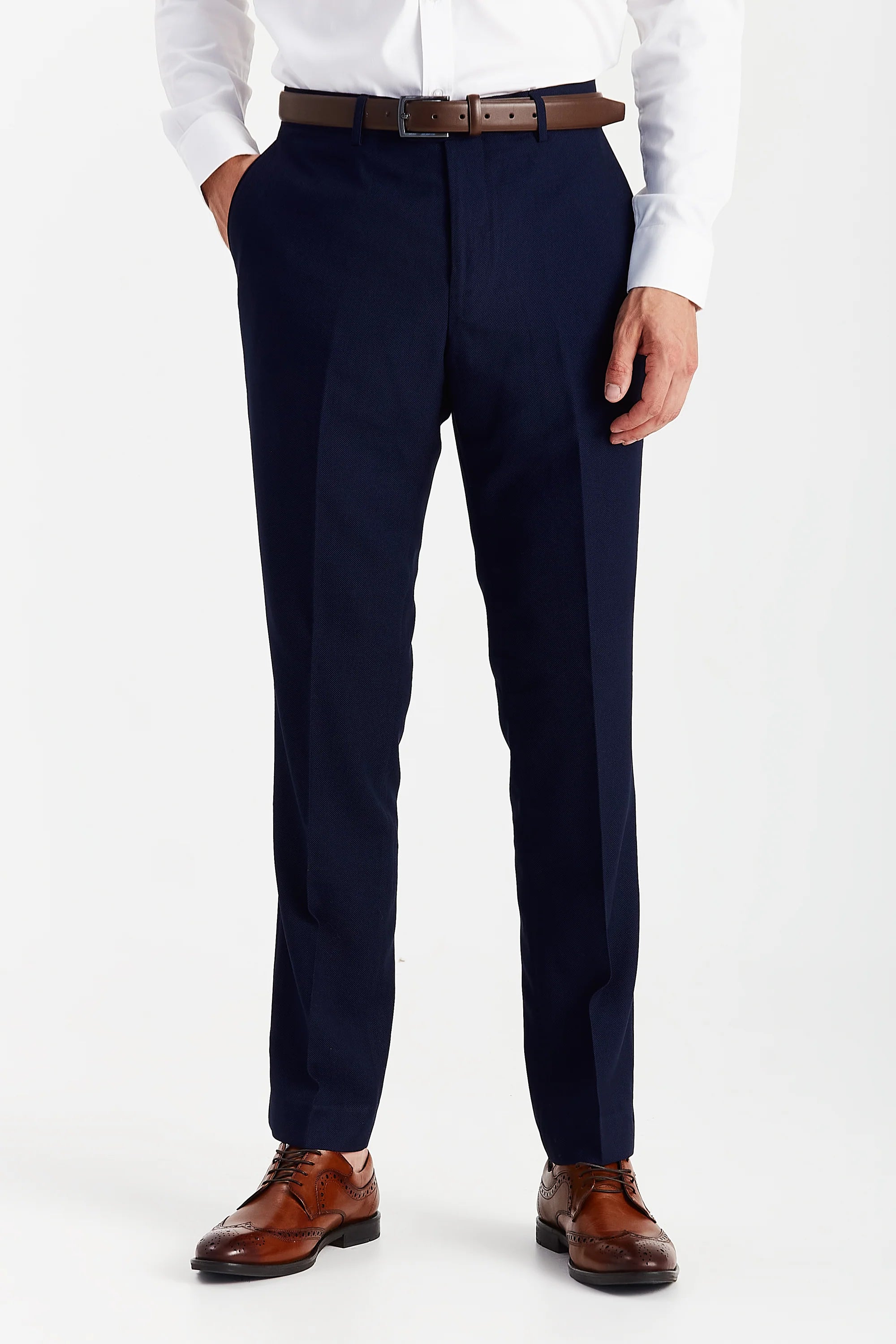 Front view of navy textured suit trousers with a brown belt, white shirt cuffs and brown brogue shoes.