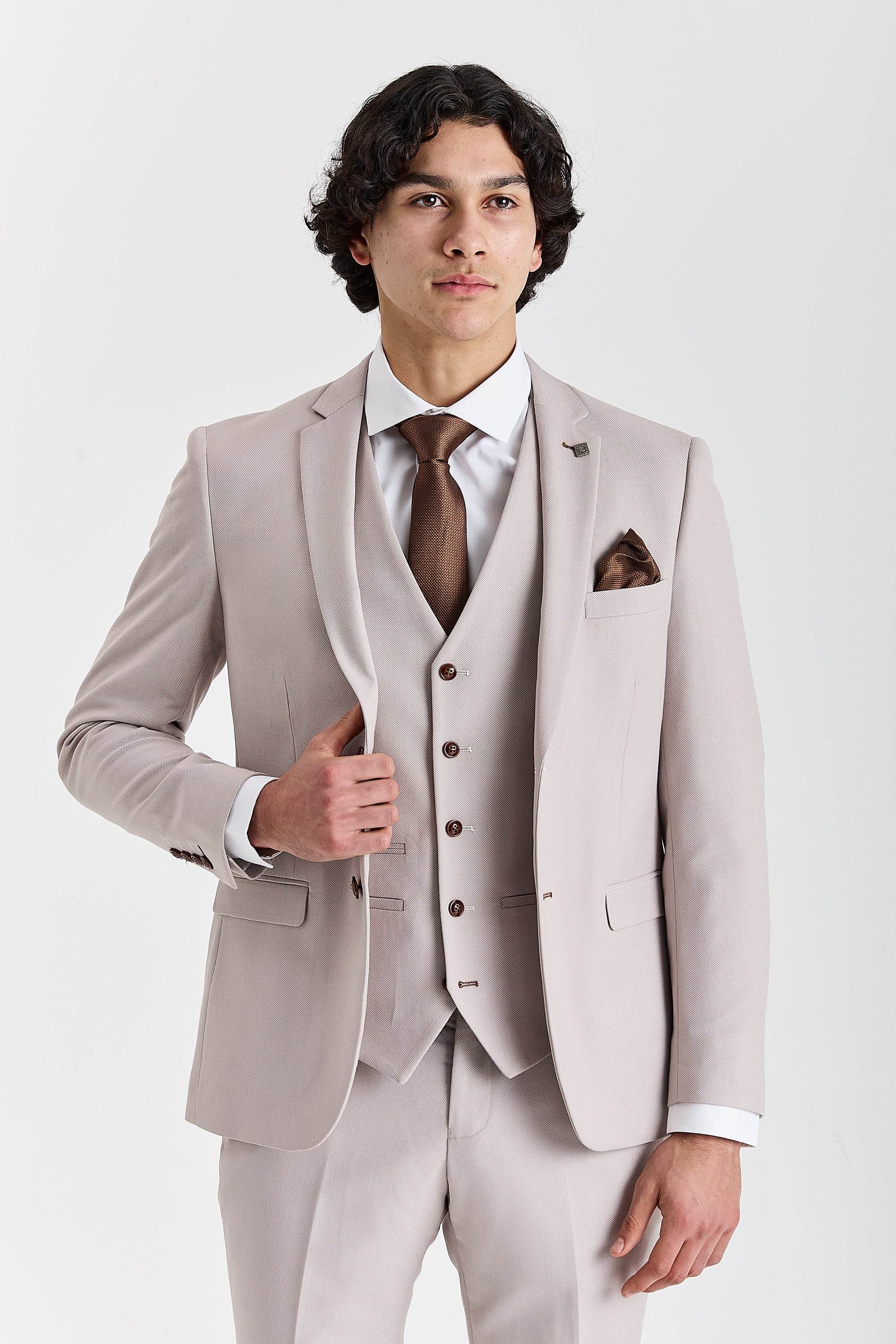 Front view of a man wearing a stone textured three piece suit, cropped above the knees, with jacket, waistcoat, trousers, white shirt, brown tie and matching pocket square.