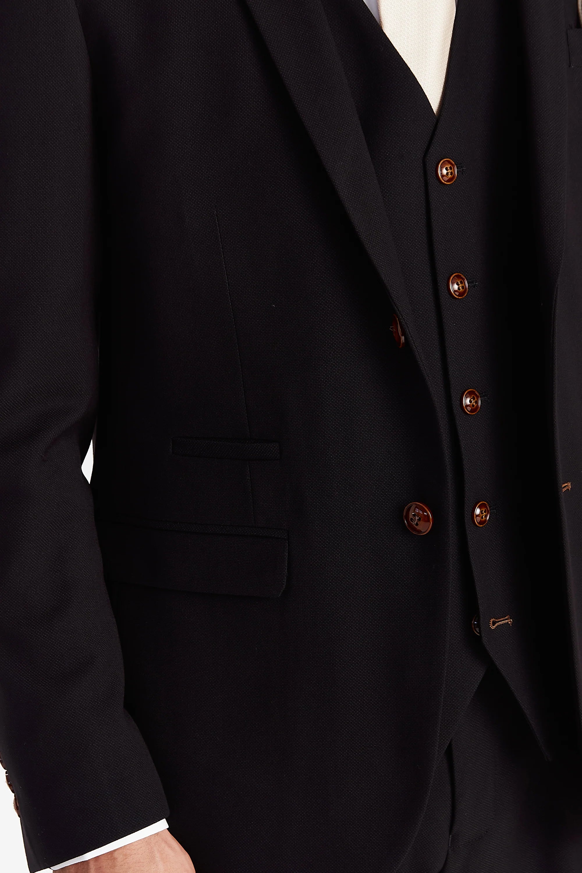 Close-up view of the black textured tailored fit blazer showing the finely woven surface, a front flap pocket, matching upper pocket trim and brown buttons on the waistcoat beneath.