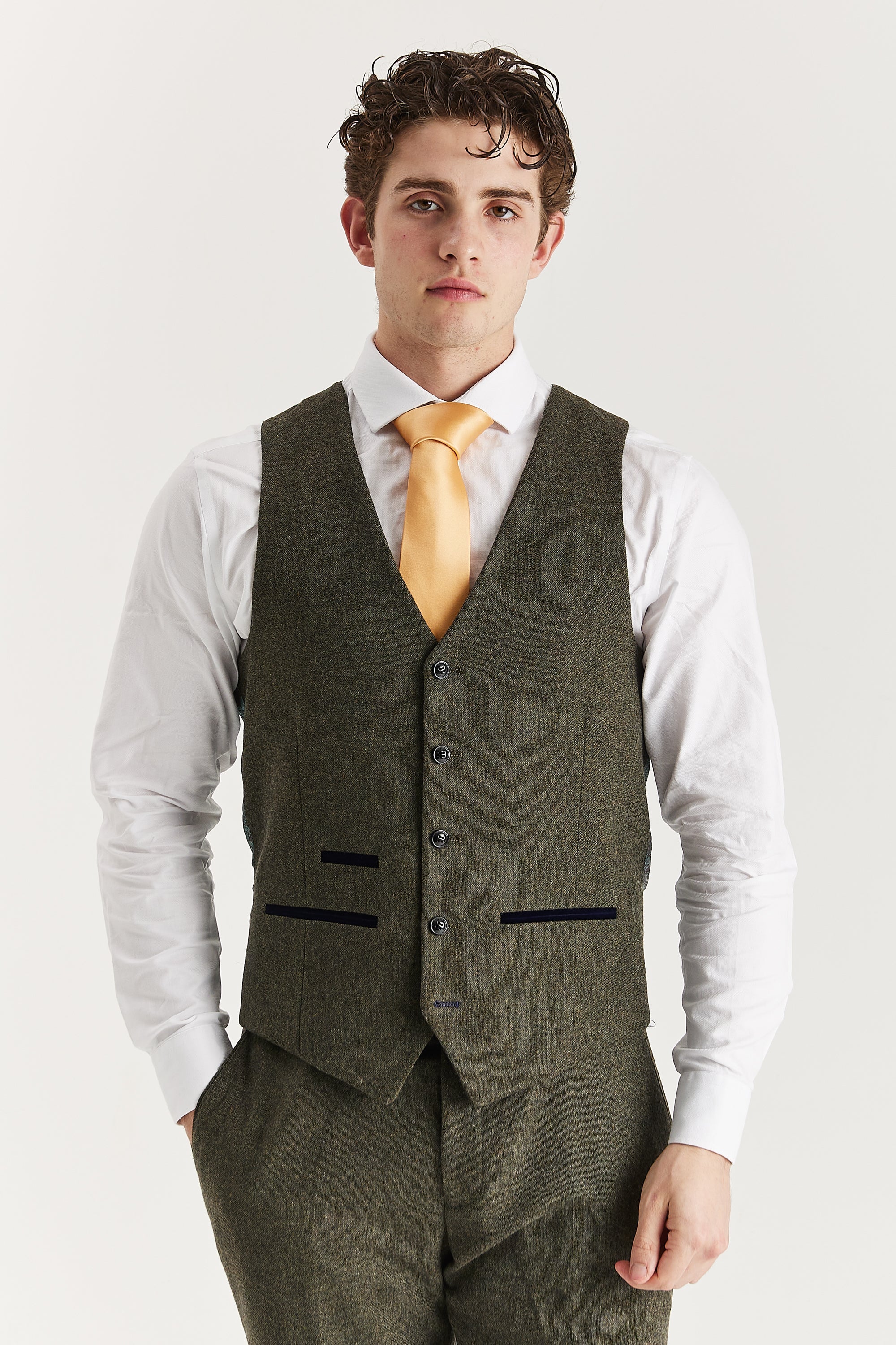 Front view of the green tweed waistcoat with contrast pocket trimmings, worn with matching trousers, a white shirt and a gold tie.