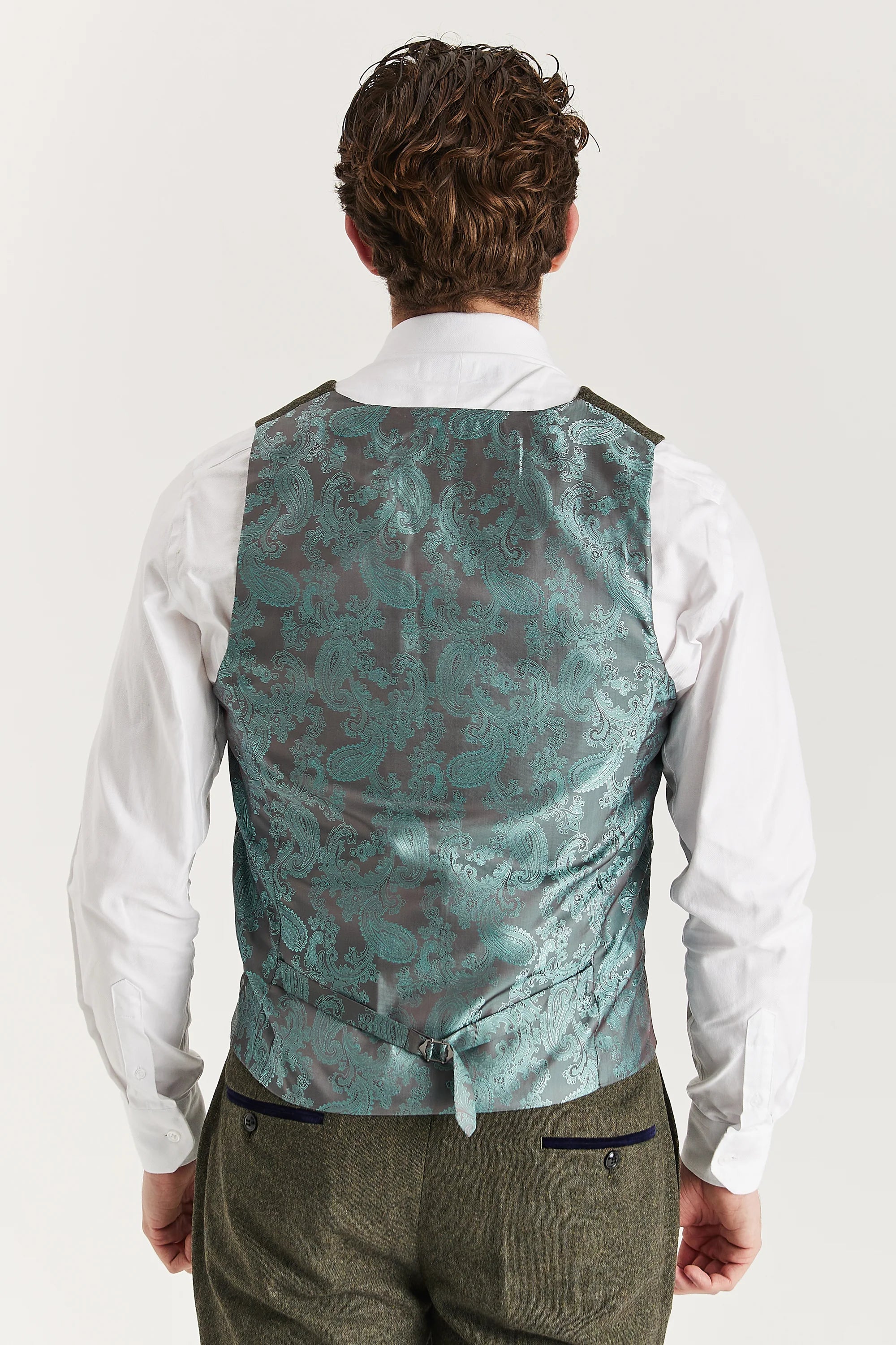 Rear view of the green waistcoat with a sage paisley back panel and adjustable strap, worn with a white shirt and matching trousers.
