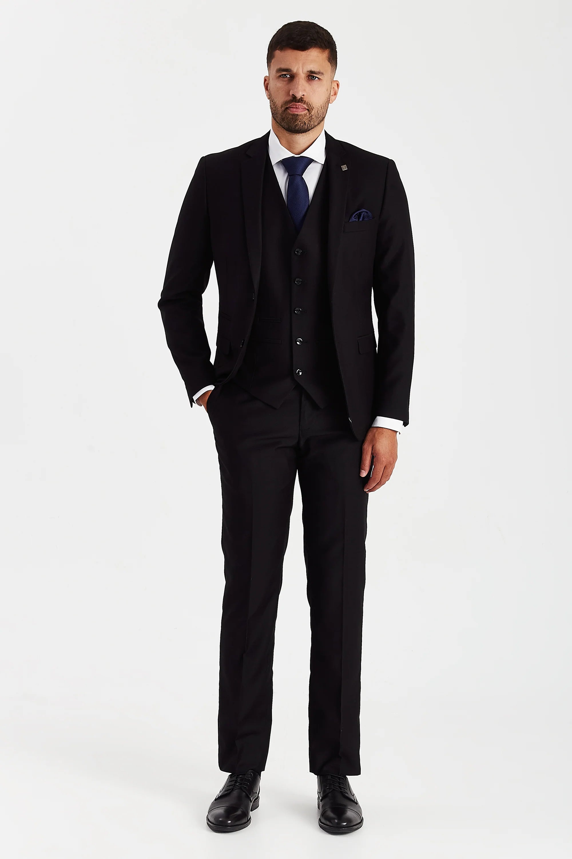Full-length front view of a man wearing a Parker black three piece suit with a white shirt, navy tie, matching pocket square and black dress shoes.