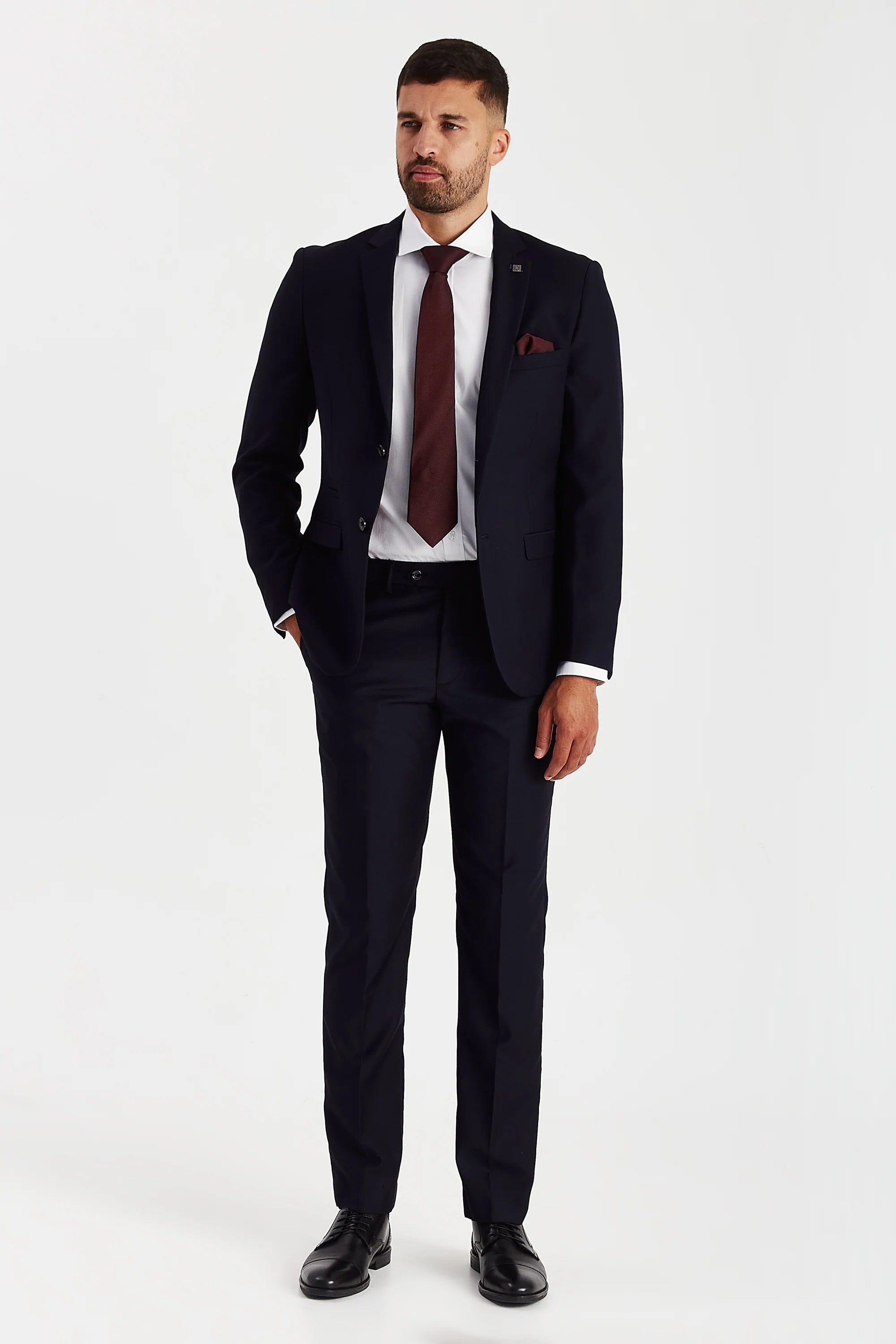 Full-length front view of a man modeling a tailored navy two-piece suit, paired with a white shirt, burgundy tie, and black shoes