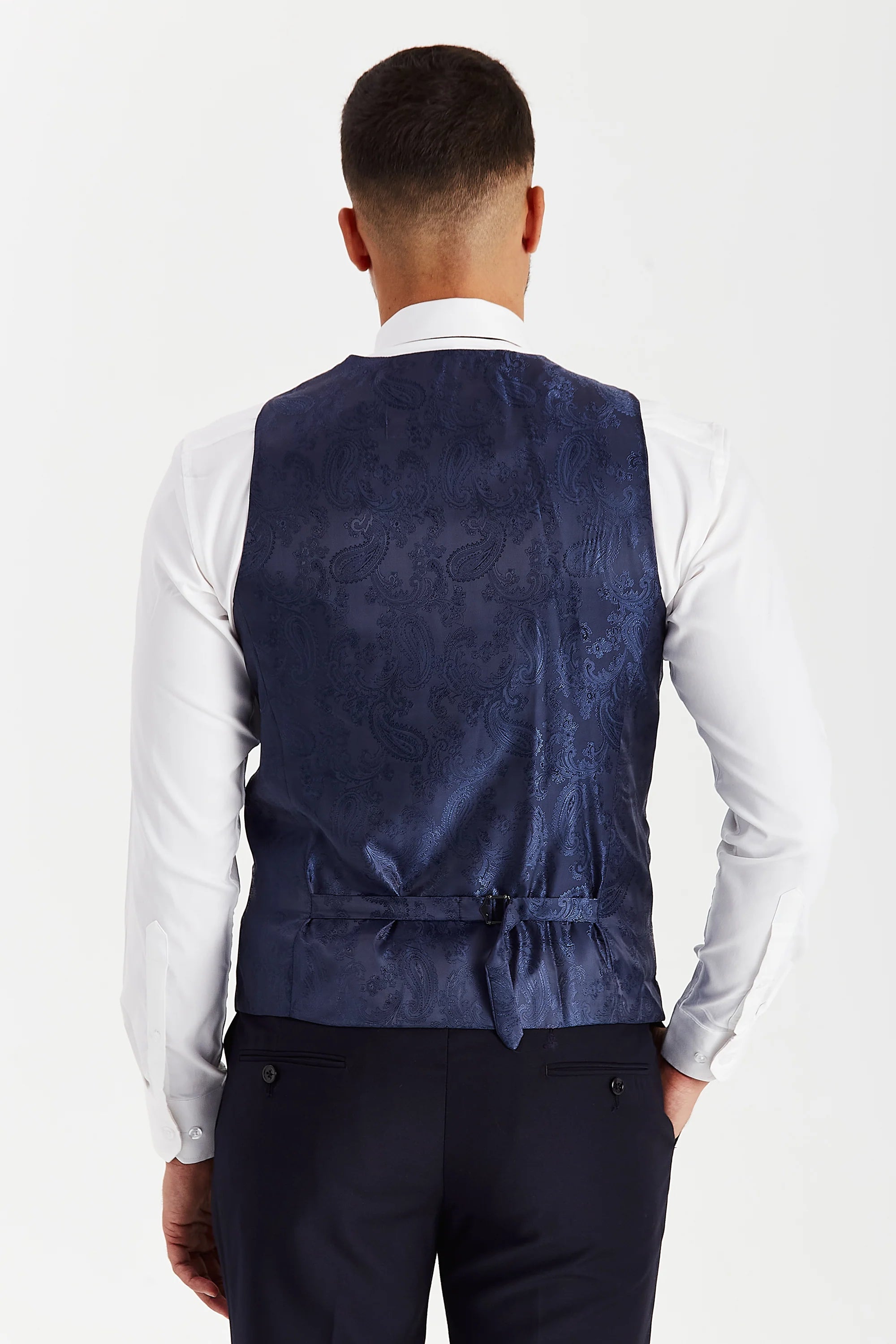 Rear view of the navy waistcoat with a blue paisley back panel and adjustable strap, worn with a white shirt and matching trousers.
