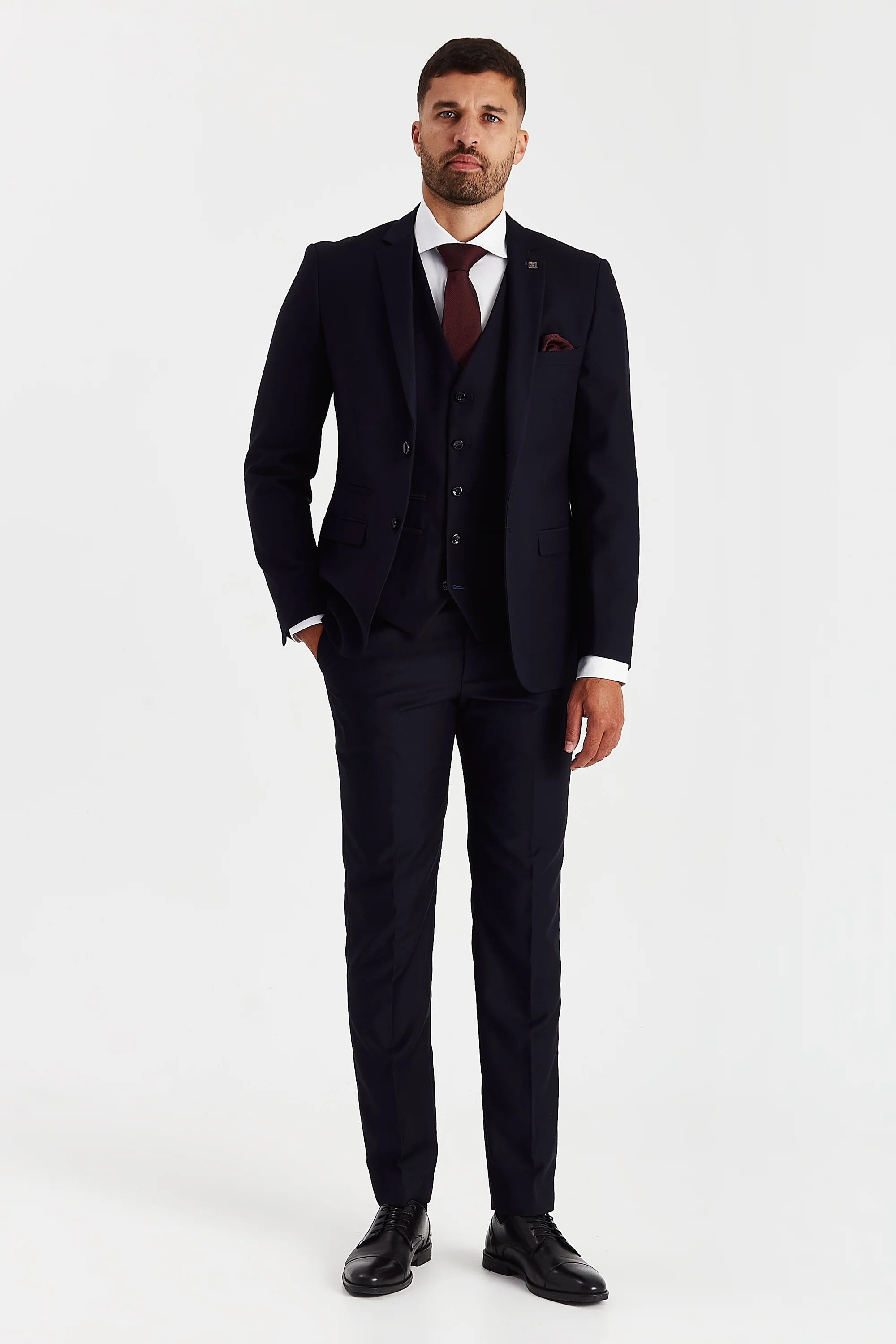 Full-length front view of a man wearing a Parker navy three piece suit with a white shirt, burgundy tie, matching pocket square and black dress shoes.