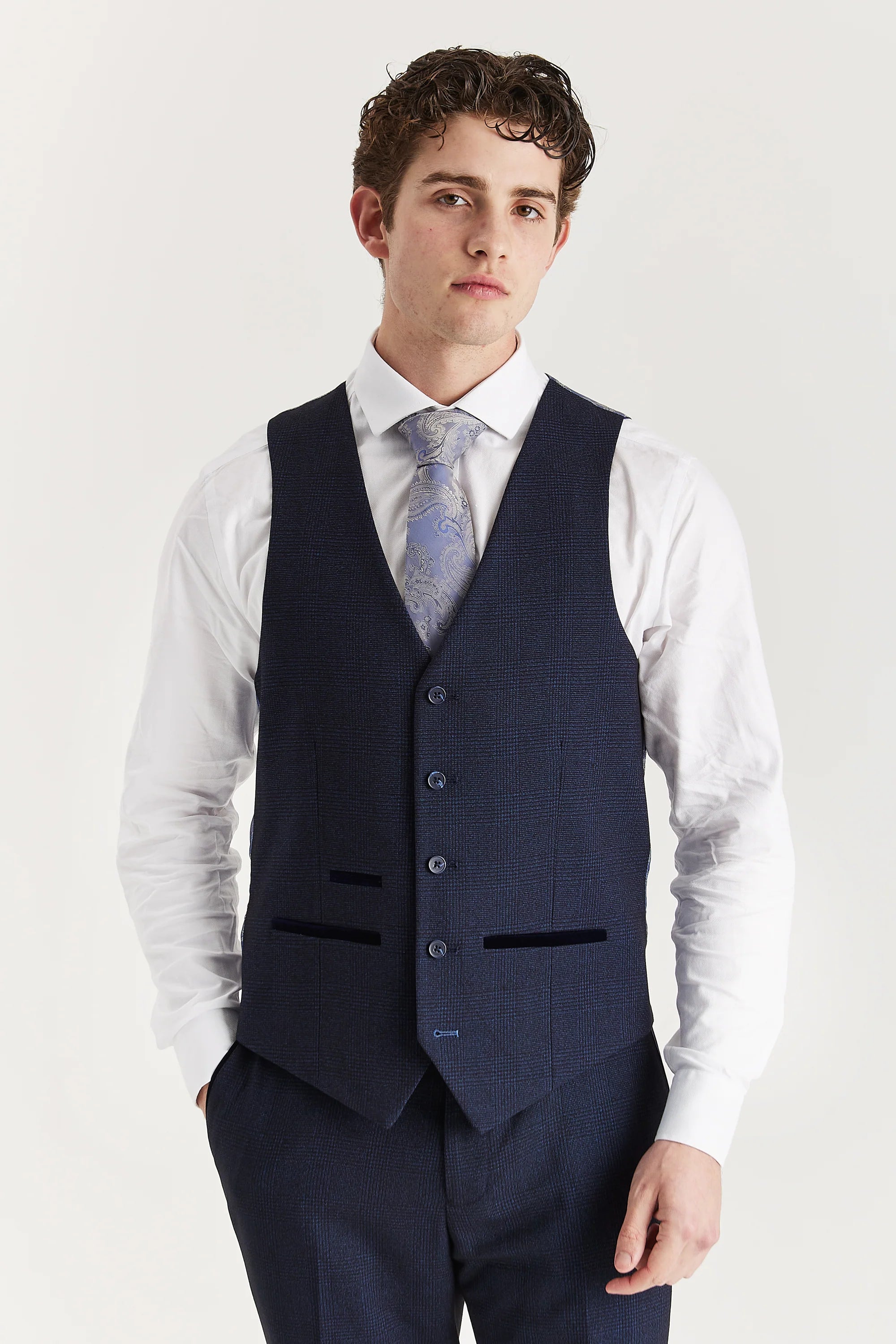 Front view of the navy glen check waistcoat with suede pocket trimmings, worn with matching trousers, a white shirt and a light blue tie.