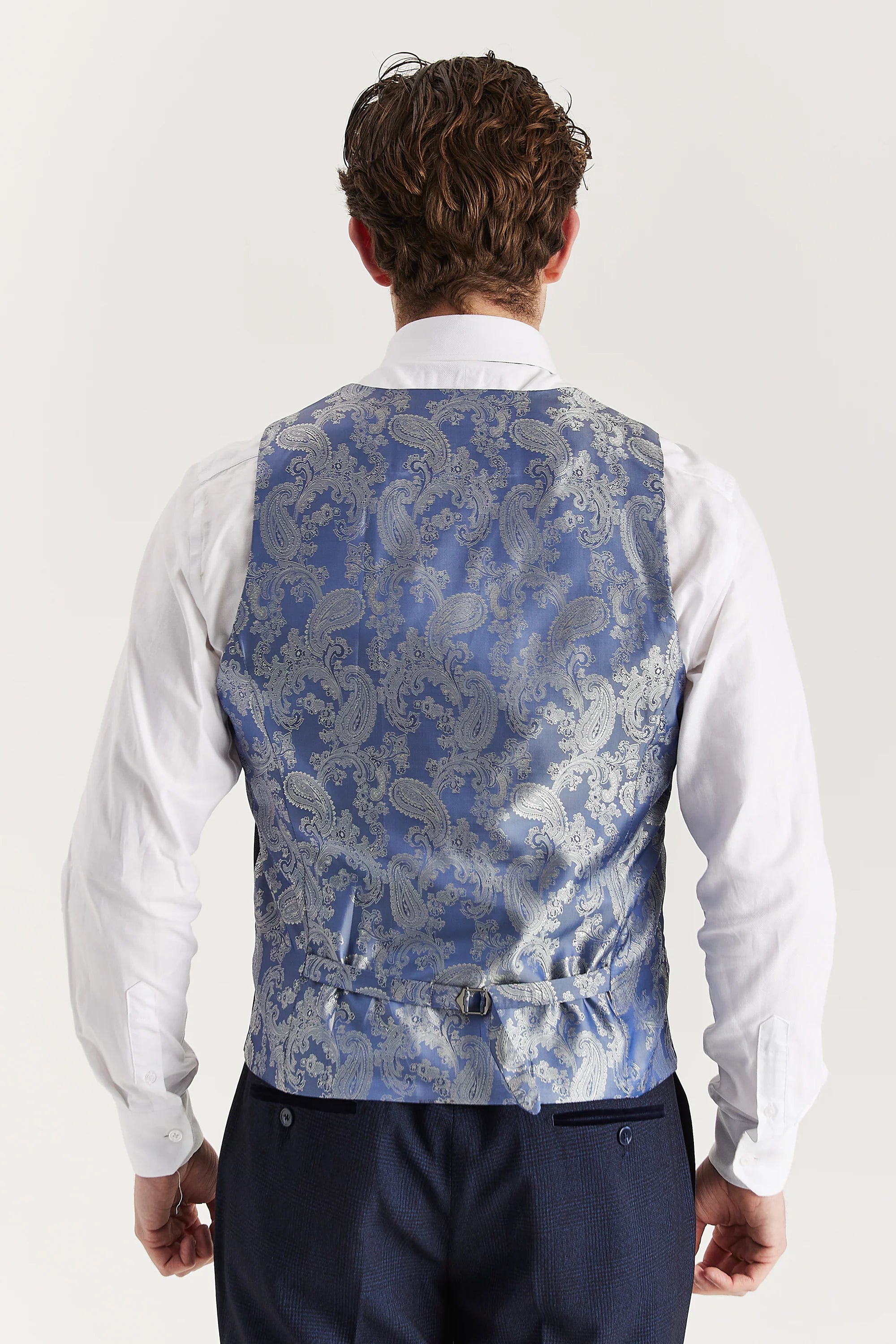 Rear view of the navy waistcoat with a paisley back panel and adjustable strap, worn with a white shirt and matching trousers.