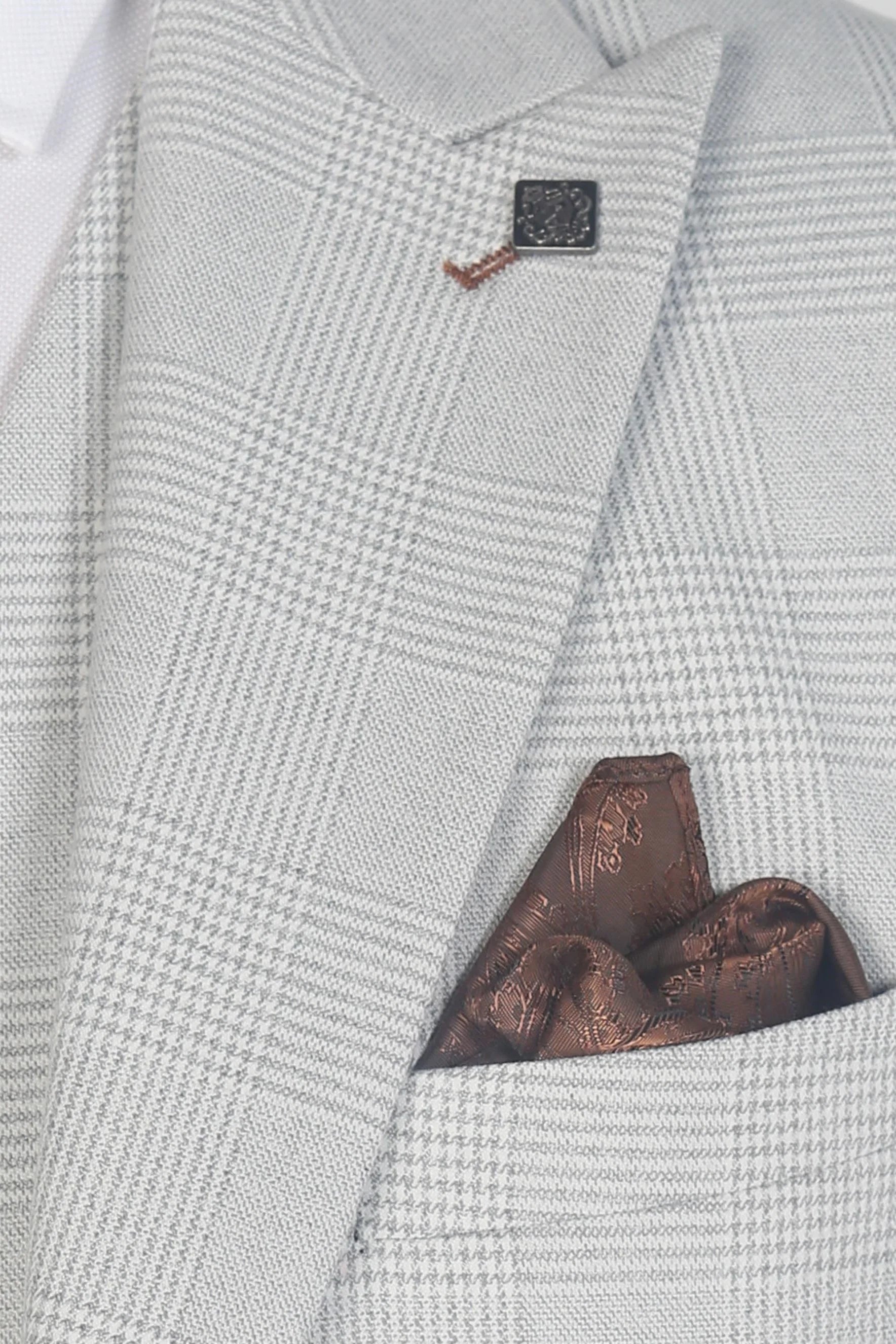 Macro close-up of the Mark stone blazer's chest , showing the detailed glen check fabric, a sharp peak lapel, a decorative lapel pin, and a matching brown pocket square.