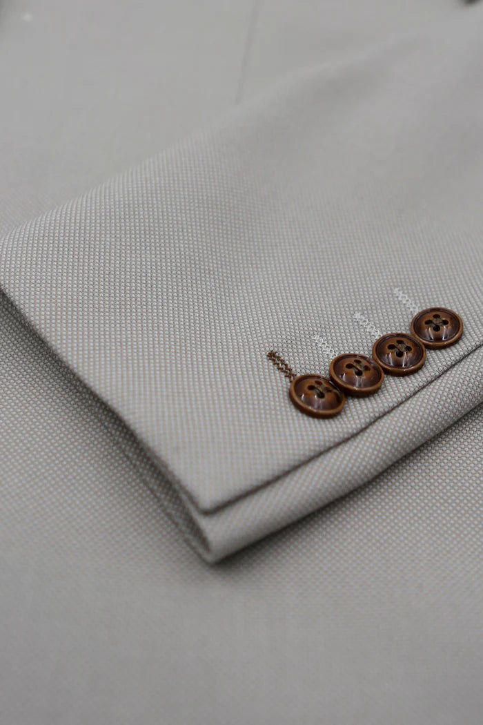 Close-up of a stone suit sleeve showcasing four brown buttons and detailed texture on the blazer cuff.