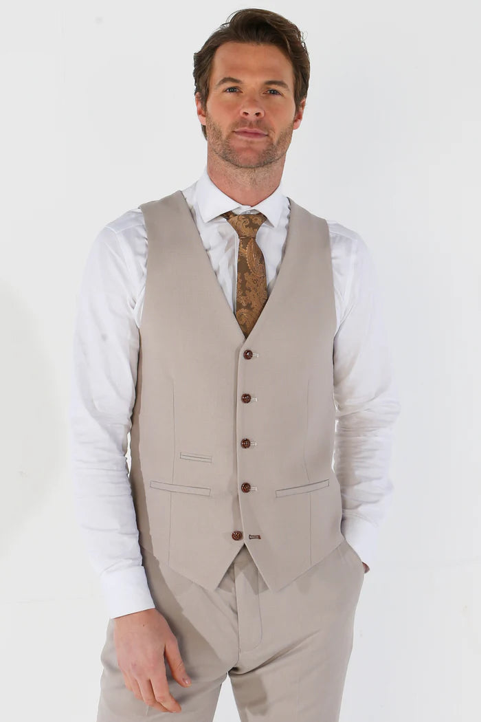 Man in a front-facing view of the stone waistcoat paired with a white shirt and gold brown paisley tie, hands in pockets.