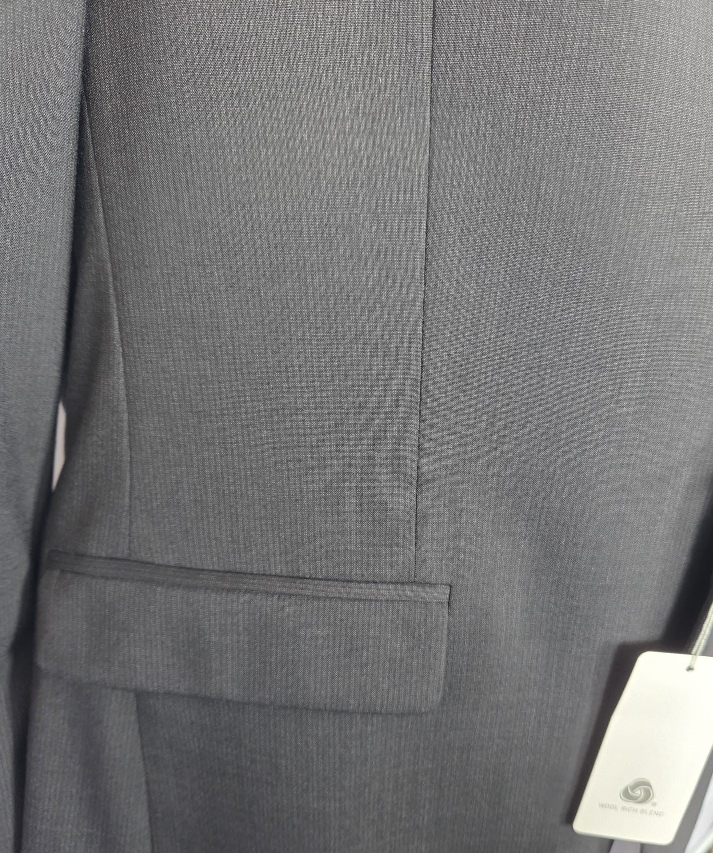 Pocket and fabric close-up showing the black micro-stripe texture of the wool-blend suit.