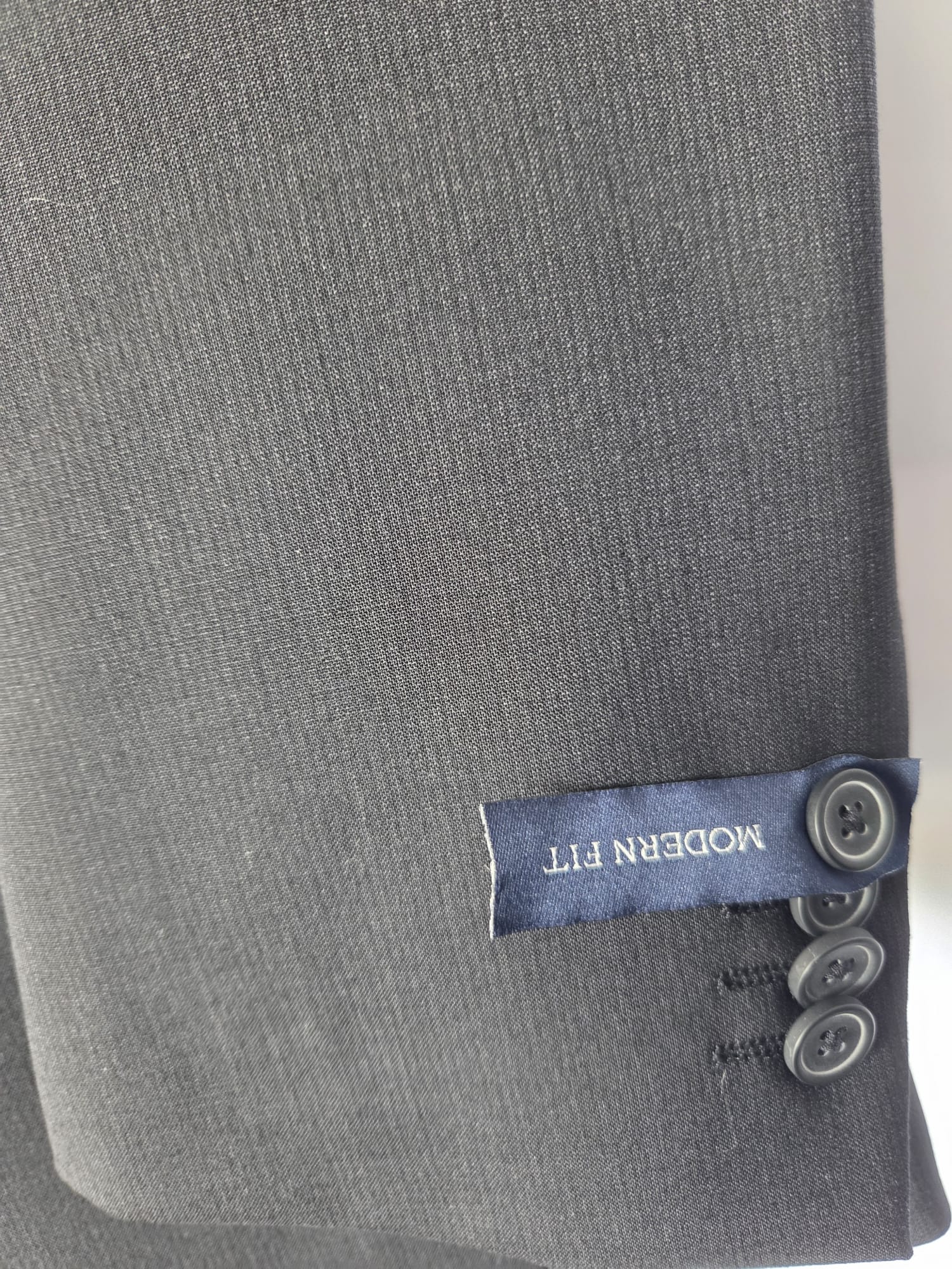 Close-up of black wool-blend suit sleeve with four-button cuff and subtle micro-stripe fabric, labeled modern fit.